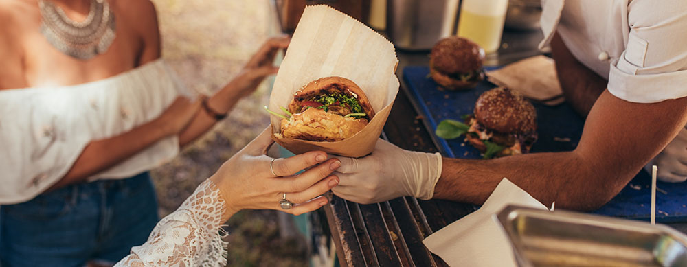 Woman hand reaching for a burger at food truck. Closeup of food truck salesman serving burger to female customer.